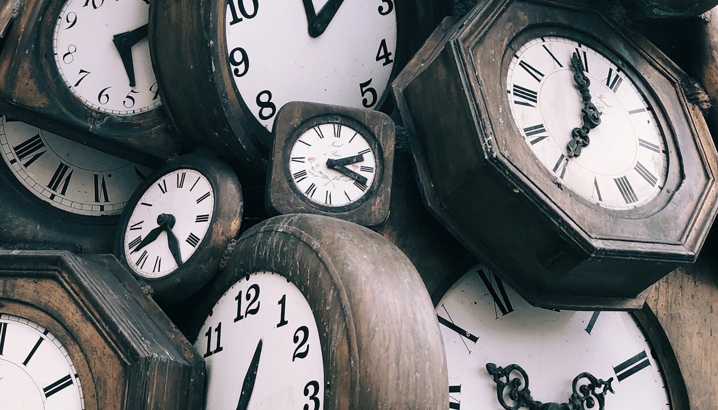 Many vintage wooden clocks stacked together showing different times