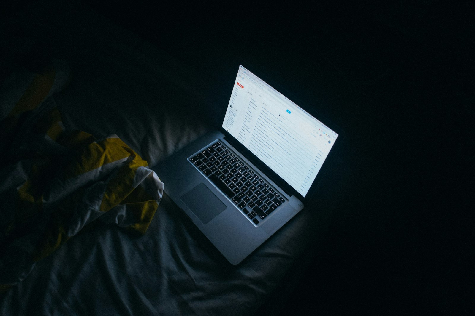 A silver and black laptop in a dark room, representing an email client rendering in dark mode