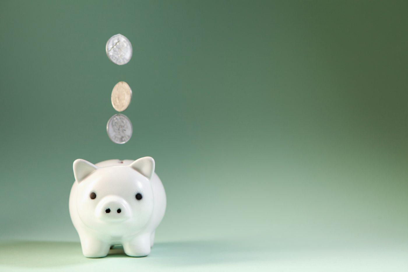 Coins falling into a white piggy bank against a green background
